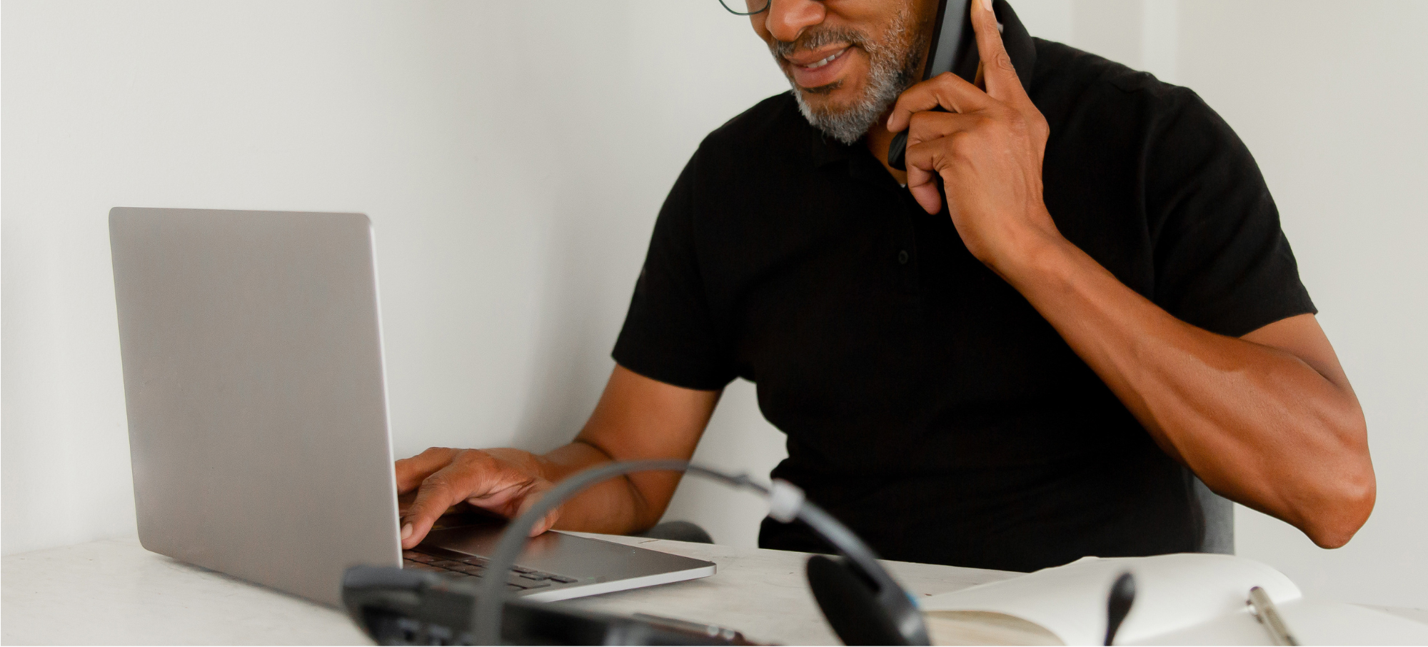 male clinician of african descent speaking on a mobile phone whilst utilising a laptop computer
